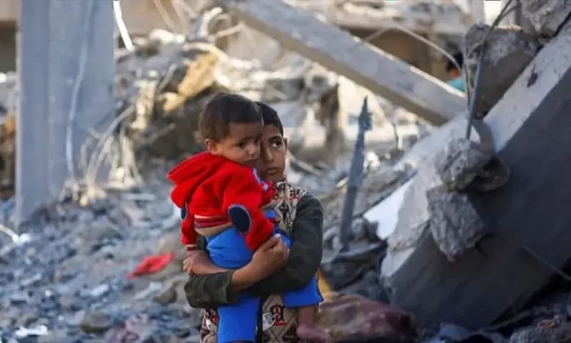 Seorang anak laki-laki Palestina sambil menggendong balita berdiri di lokasi serangan Israel saat konflik yang sedang berlangsung antara Israel dan kelompok perlawanan Palestina Hamas di Rafah, di selatan Jalur Gaza, Senin (4/12/2023).(Foto: Dok. Antara)